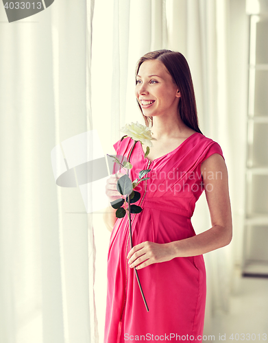 Image of happy pregnant woman with rose flower at home