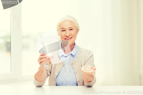 Image of happy senior woman with water and medicine at home