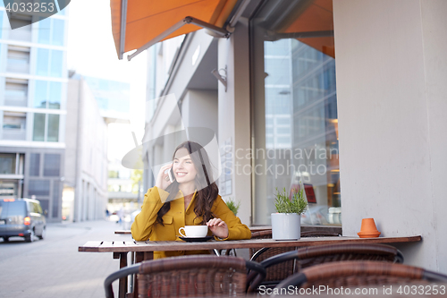 Image of happy woman calling on smartphone at city cafe
