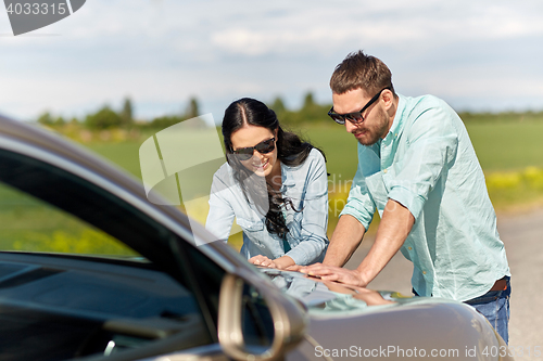 Image of happy man and woman with road map on car hood