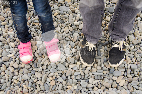 Image of Two pairs of feet in sneakers, adults and children, are on the pebble