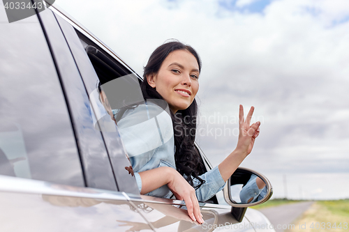 Image of happy woman driving in car showing peace sign