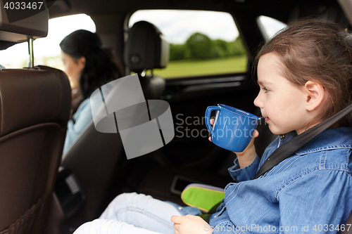 Image of little girl driving in car and drinking from cup