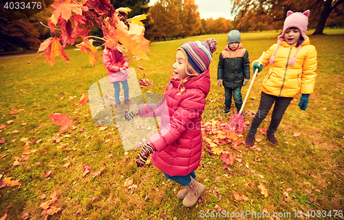 Image of happy children playing with autumn leaves in park