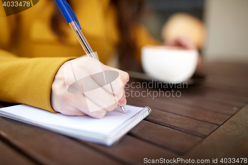 Image of close up of hand writing to notebook at cafe