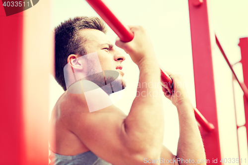 Image of young man exercising on horizontal bar outdoors