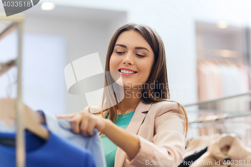 Image of happy young woman choosing clothes in mall