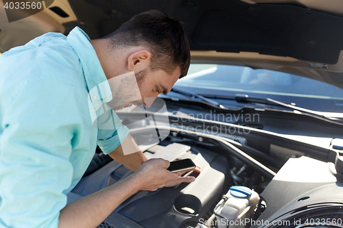 Image of man with smartphone and broken car at countryside