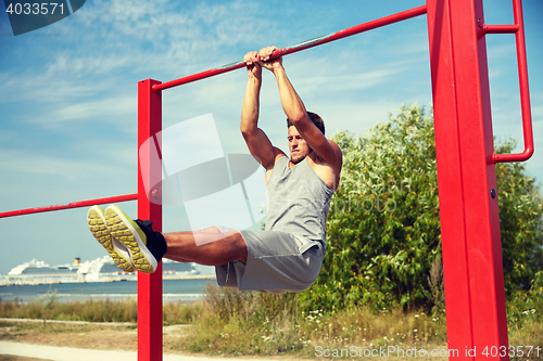 Image of young man exercising on horizontal bar outdoors