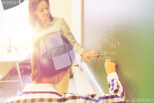 Image of school boy with teacher writing on chalk board