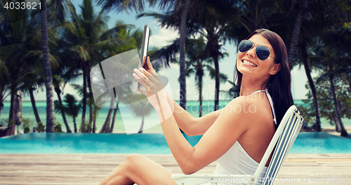 Image of smiling woman with tablet pc sunbathing on beach