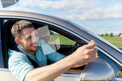 Image of happy smiling man with smartphone driving in car