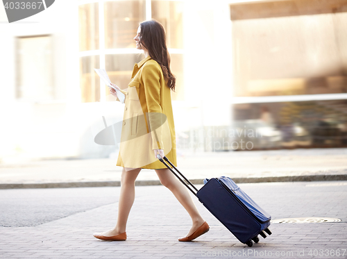 Image of happy young woman with travel bag and map in city