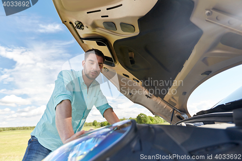 Image of man with open hood of broken car at countryside