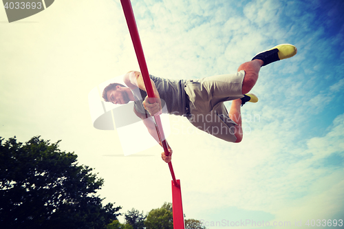 Image of young man exercising on horizontal bar outdoors