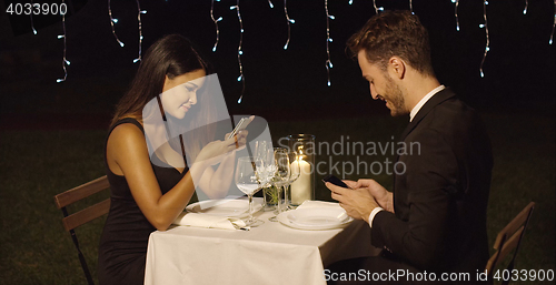 Image of Young couple checking their mobiles during dinner