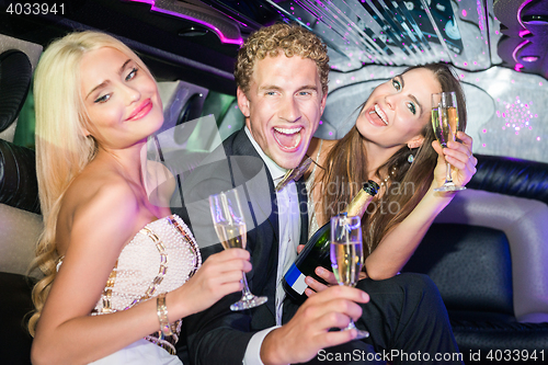 Image of Excited young man with women holding champagne flutes in limousi
