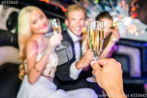 Image of Closeup of hand toasting champagne flute with friends in limousi