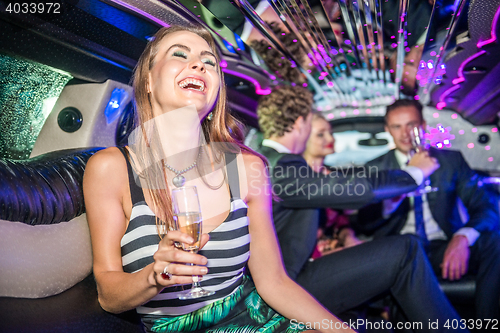 Image of Cheerful young woman holding champagne flute while friends celeb