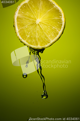 Image of Lime slice and splash of juice isolated on green background.