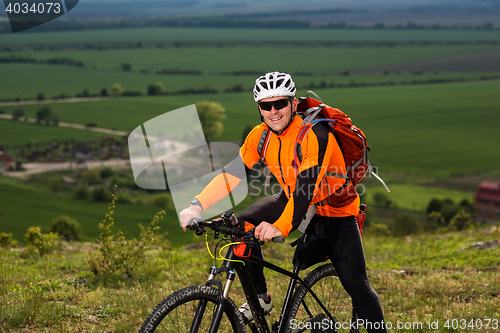 Image of Young man cycling on a rural road through green meadow