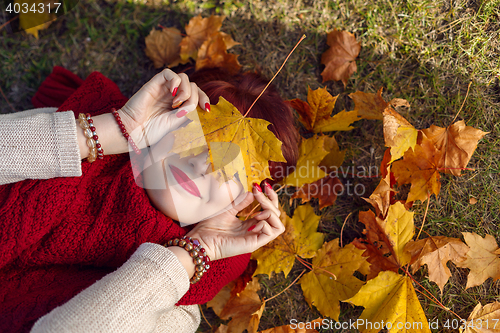 Image of Red hair girl lying with autumn maple leaf