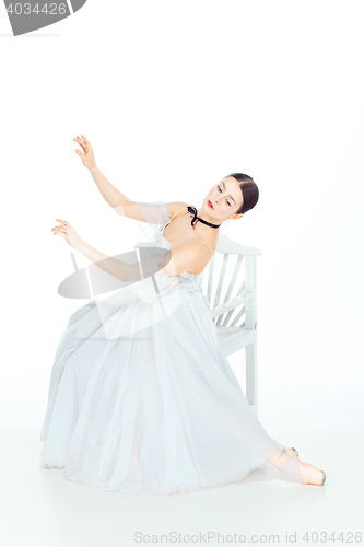 Image of Ballerina in white dress sitting, studio background.