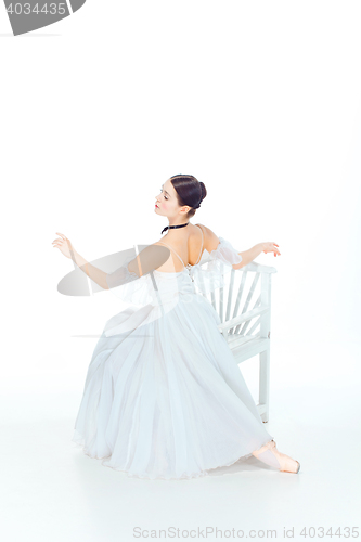 Image of Ballerina in white dress sitting, studio background.