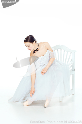 Image of Ballerina in white dress sitting, studio background.