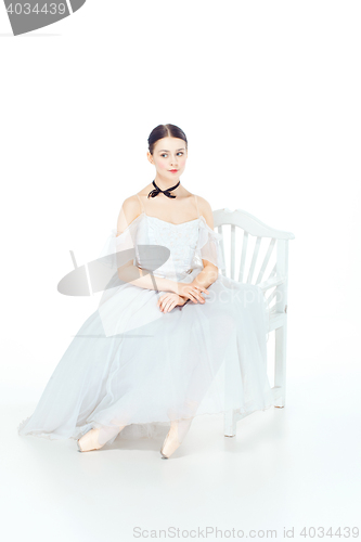 Image of Ballerina in white dress sitting, studio background.