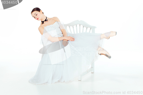 Image of Ballerina in white dress sitting, studio background.