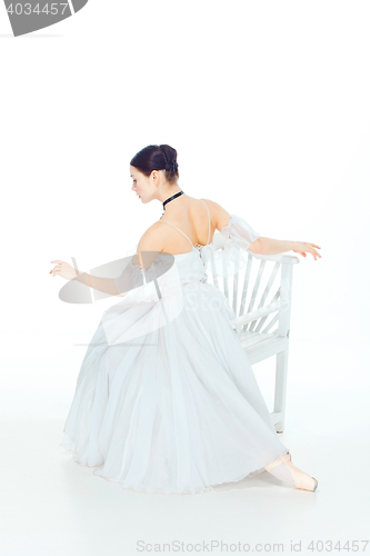 Image of Ballerina in white dress sitting, studio background.