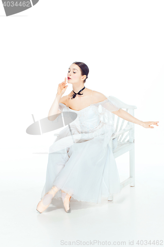 Image of Ballerina in white dress sitting, studio background.