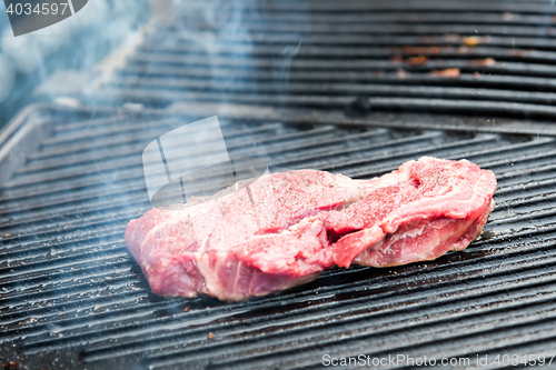 Image of raw steak with spices on metal grill