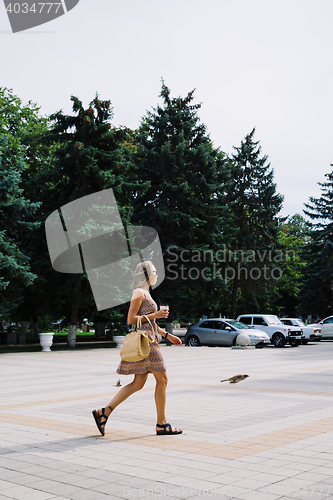 Image of Young brunette woman with coffee cup walking in city