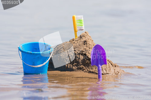 Image of Construction of a sand castle, next to which stands a shovel and bucket on the shallows of the river