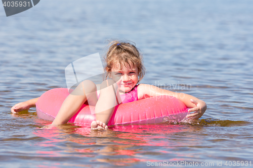 Image of Five-year girl swims in the river sat on the lap swimming and happily looks into the frame