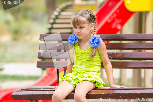 Image of Portrait of upset five year old girl who is sitting on the bench on the background of the playground