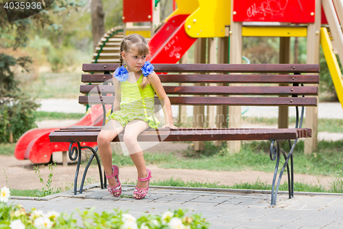 Image of Upset girl bit her lip while sitting on the bench on the background of the playground