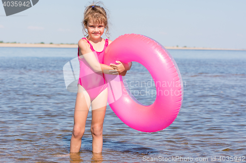 Image of Five-year girl in a pink bathing suit standing with swimming laps in the river