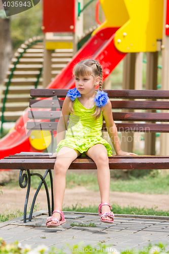 Image of Upset girl sitting on the bench on the background of the playground