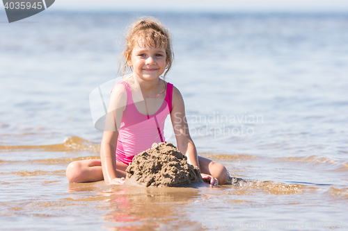 Image of Five-year girl in a pink bathing suit playing in the sand in the shallows of the river