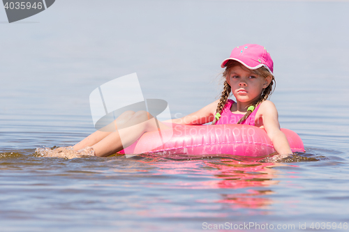 Image of Sad girl in a cap floating in the river sat on the swimming circle