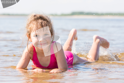 Image of Five-year girl lies in water in the shallows of the river and looking at the frame
