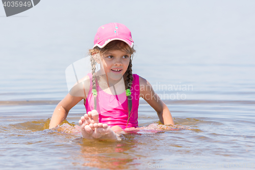 Image of Girl in a cap sits on a shallow river in water