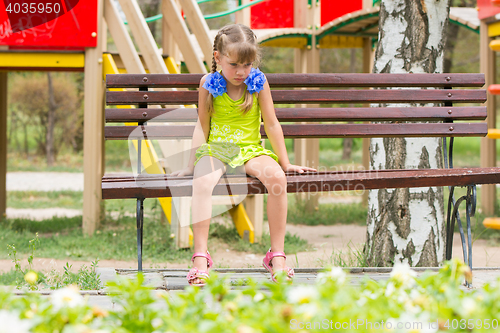 Image of Crying girl sitting on the bench on the background of the playground