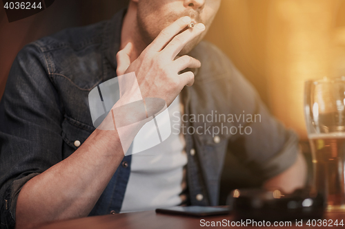 Image of man drinking beer and smoking cigarette at bar