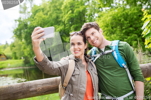 Image of couple with backpacks taking selfie by smartphone
