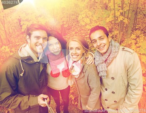 Image of smiling friends taking selfie in autumn park