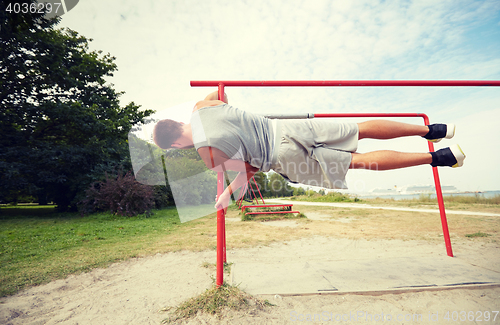Image of young man exercising on parallel bars outdoors
